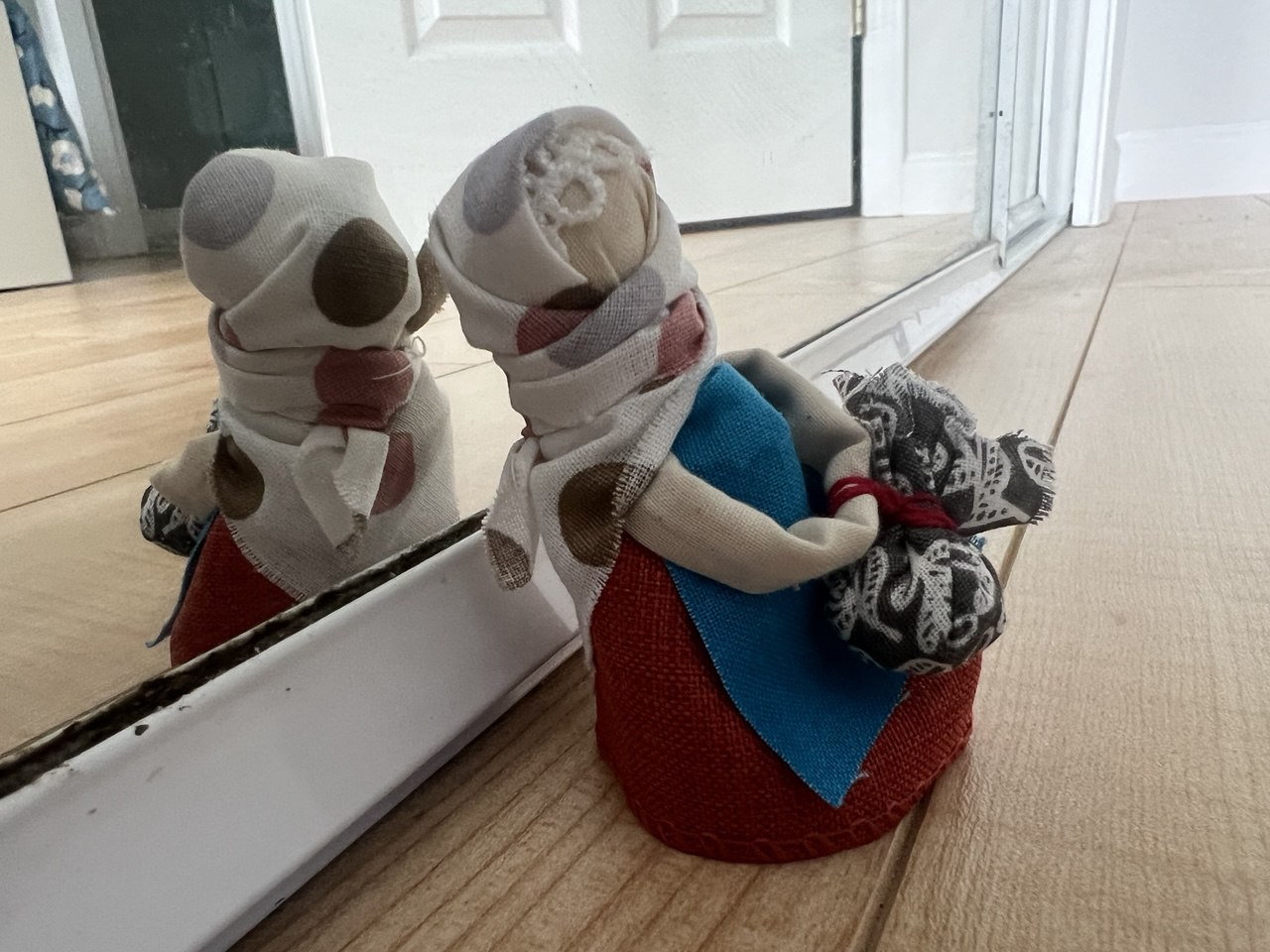 A small handmade doll standing in front of a mirror